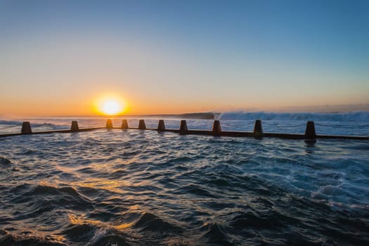 Ocean waves crashing breaking on shallow reefs and washing along beach coastline into concrete tidal pool with power and energy of nature