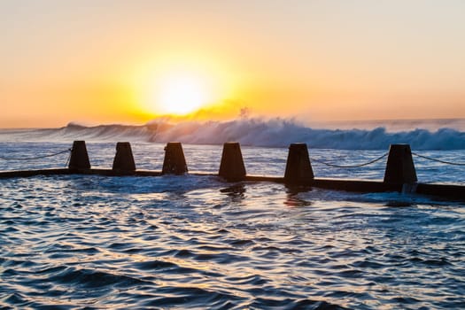 Ocean waves crashing breaking on shallow reefs and washing along beach coastline into concrete tidal pool with power and energy of nature