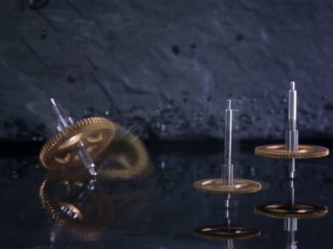 Close-up three fast-rotating gears on water-covered slate slab