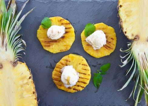 Grilled pineapple rings with ice cream balls and honey on slate plate