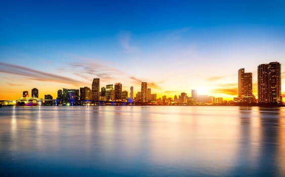 Miami city skyline panorama at dusk with urban skyscrapers over sea with reflection
