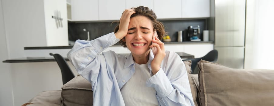 Image of frustrated woman on phone call, listens to bad news during telephone conversation, sits at home, feels disappointed and upset.