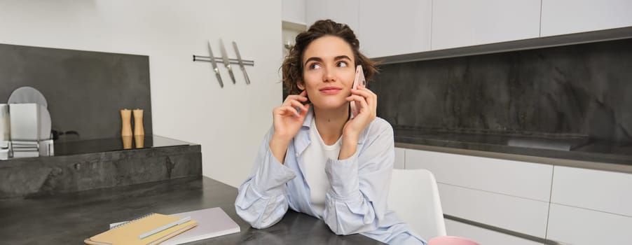 Portrait of cute smiling girl talks on mobile phone, sits at home and calls someone with smartphone.