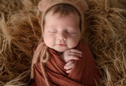 Newborn baby girl swaddled in white fabric sleeping in basket decorated with pumpkins. Infant child kid napping on fur autumn studio portrait