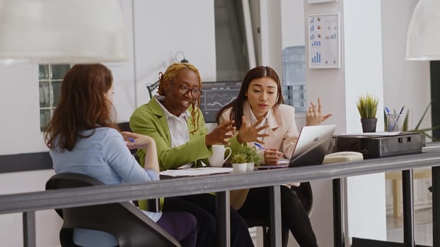 Diverse team of coworkers doing collaboration in office to plan annual report, checking online analytics on files in coworking space. Female workers discussing corporate growth. Tripod shot.