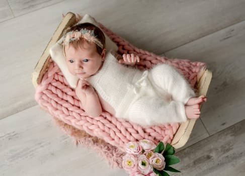 Adorable newborn baby girl lying in tiny bed on fur portrait. Cute infant child kid swaddled in fabric resting in room with daylight