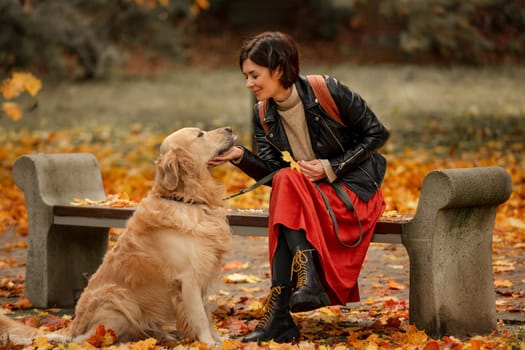 A young woman sitting on a bench in an autumn park and petting a Golden Retriever dog