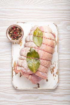 Raw wrapped rolled sliced pork with bay leaf and seasonings on white cutting board on rustic white wooden background top view. Pork roll ready to be prepared.