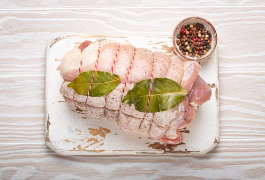 Raw wrapped rolled sliced pork with bay leaf and seasonings on white cutting board on rustic white wooden background top view. Pork roll ready to be prepared.