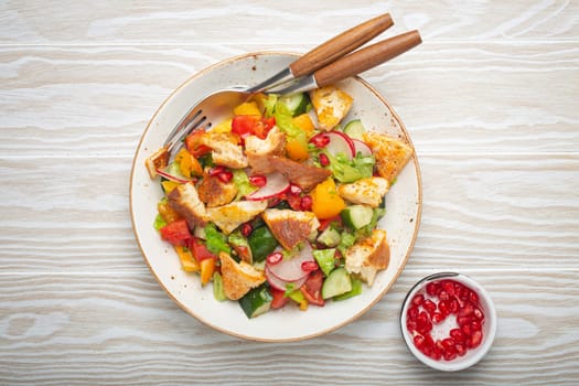 Traditional Levant dish Fattoush salad, Arab cuisine, with pita bread croutons, vegetables, herbs. Healthy Middle Eastern vegetarian salad, rustic wooden white background top view.