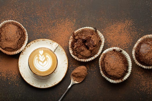 Chocolate and cocoa browny muffins with coffee cappuccino in cup top view on brown rustic stone background, sweet homemade dark chocolate cupcakes.