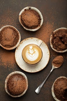 Chocolate and cocoa browny muffins with coffee cappuccino in cup top view on brown rustic stone background, sweet homemade dark chocolate cupcakes.