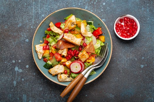 Traditional Levant dish Fattoush salad, Arab cuisine, made with pita bread croutons, vegetables and herbs. Healthy Middle Eastern vegetarian salad on plate, rustic dark blue background top view.