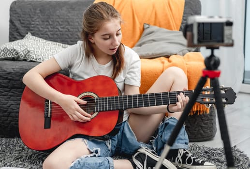 Girl teenager with guitar recording streaning online lesson with camera for blog followers in social media. Young musician guitarist filming vlog with tutorial