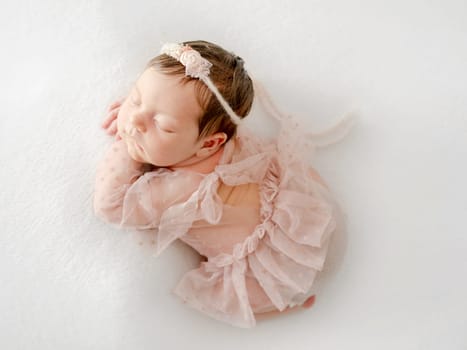 Adorable newborn baby girl sleeping on pillow. Cute infant child kid in pink dress and wreath napping lying on tummy