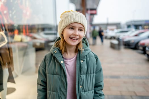 Preteen girl smiling at street portrait in city with blurred background. Cute female child kid wearing hat outdoors at autumn time