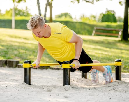 Man doing push ups with horizontal bar outdoors in park for healthy wellbeing. Sportsman guy making strong workout for muscle