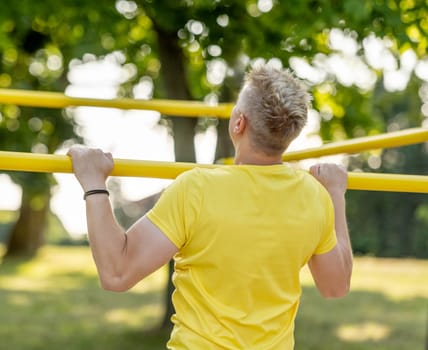 Man doing push ups with horizontal bar outdoors in park for healthy wellbeing. Sportsman guy making strong workout for muscle