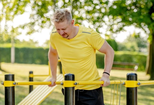 Man doing push ups with horizontal bar outdoors in park for healthy wellbeing. Sportsman guy making strong workout for muscle