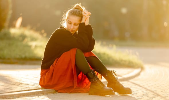 Beautiful teenager girl in red skirt sitting outdoors at street. Pretty teen model posing in trendy clothes