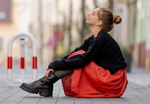 Beautiful teenager girl in red skirt sitting outdoors at street. Pretty teen model posing in trendy clothes