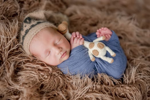 Adorable newborn baby boy smiling during sleeping and holding knitted giraffe toy. Cute infant child kid napping on fur