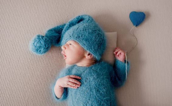 Adorable newborn baby boy in knitted hat and clothes holding heart toy and looking back. Cute infant child kid studio portrait