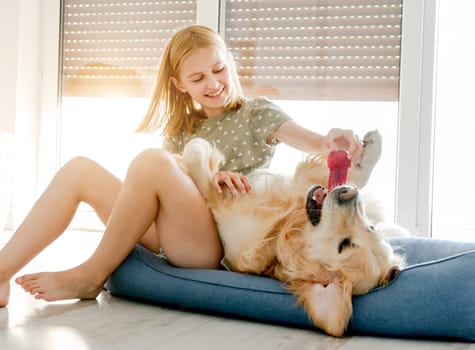 Cute preteen child girl with golden retriever dog playing at pillow at floor together. Pretty female kid with doggy pet labrador and toy at home