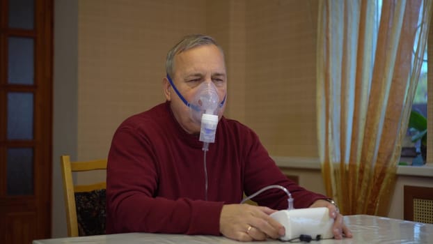 An elderly man puts on an inhaler mask. A man does a respiratory procedure at home. 4k