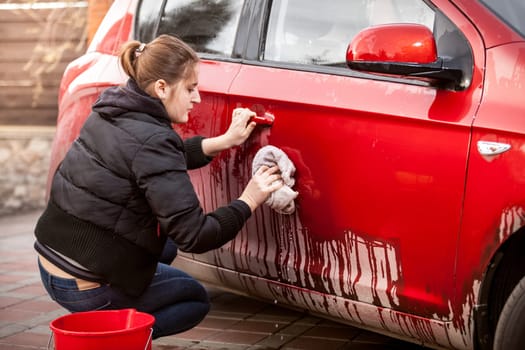 Beautiful woman cleaning car door from mud and dirt