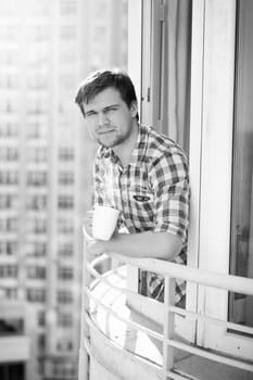 Black and white portrait of man with cup of coffee on balcony