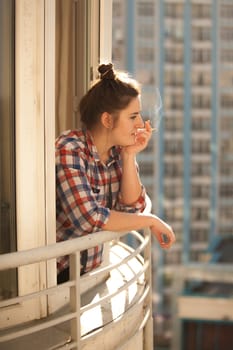 Toned photo of hipster girl smoking out of widow