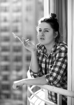 Black and white closeup portrait of young woman smoking on balcony