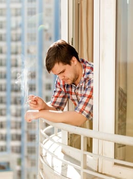 Closeup photo of depressed man smoking cigarette out of window