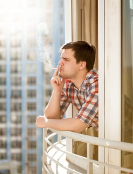 Closeup portrait of young man smoking cigarette out of window