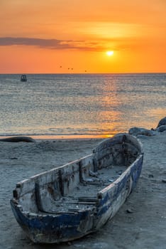 Old damaged wooden canoe with a beautiful orange sunset in the background in Santa Marta, Colombia