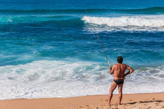 Fishermen casting bait from beach into blue ocean waters on summer afternoon