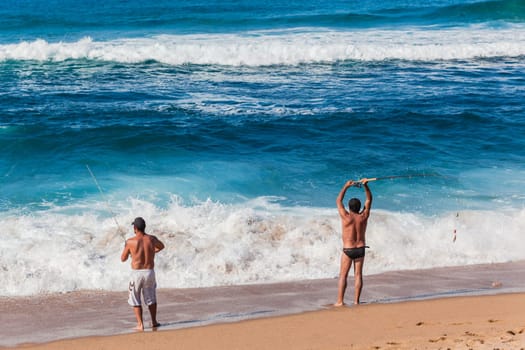 Fishermen casting bait from beach into blue ocean waters on summer afternoon