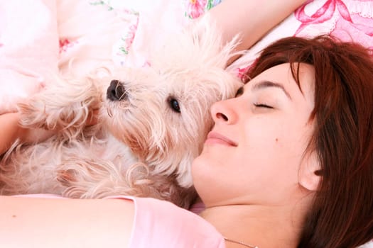 Westie sleeping next to woman in bed .