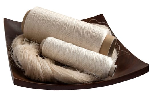 Raw natural silk yarn skein and bobbins in wooden platter isolated on white background