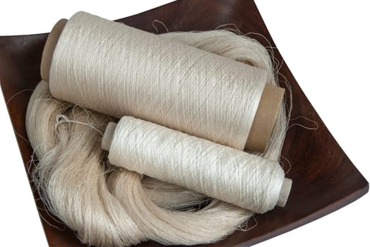 Raw natural silk yarn skein and bobbins in wooden platter isolated on white background