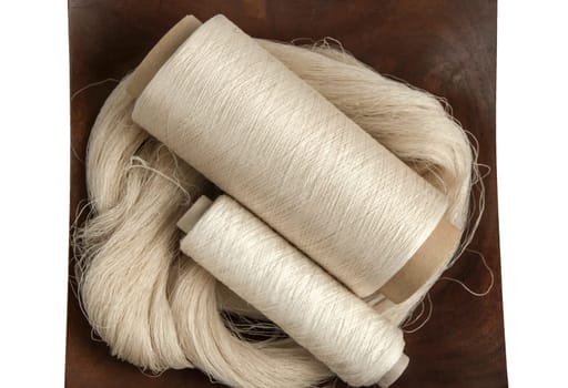 Raw natural silk yarn skein and bobbins in wooden platter isolated on white background