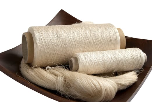 Raw natural silk yarn skein and bobbins in wooden platter isolated on white background