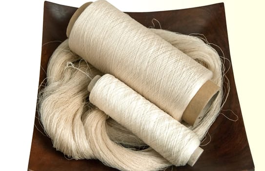 Raw natural silk yarn skein and bobbins in wooden platter isolated on white background