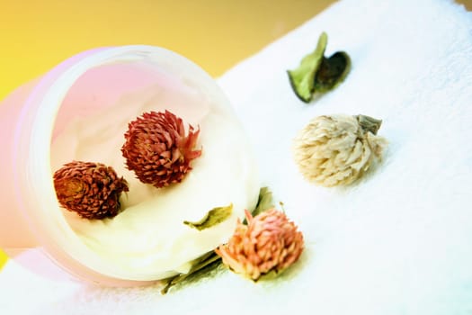 Spa essentials (cream, white towel and pink flowers) isolated on yellow