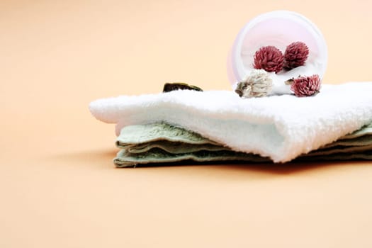 Spa essentials (cream, white towel and pink flowers) isolated on yellow