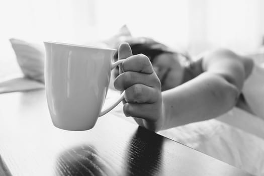 Black and white portrait of woman in bed taking cup from table