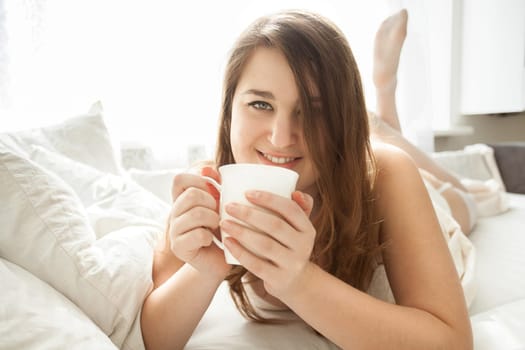 Beautiful smiling woman drinking coffee in bed at morning