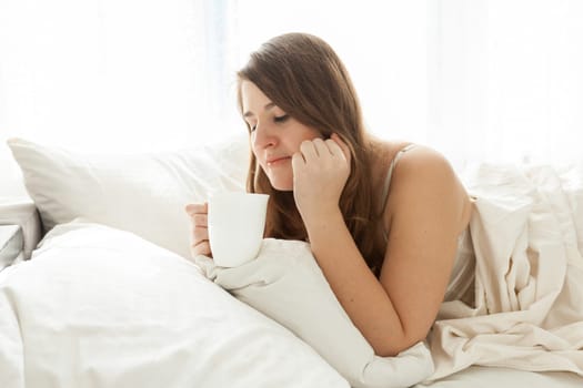 Portrait of cute woman lying in bed with cup of coffee