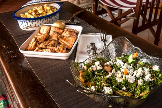 Rustic table with dishes of grilled salmon, salad and sauteed potatoes